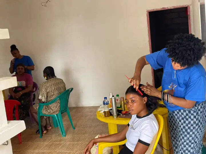 A student styling a client's hair with a comb while other students work behind her